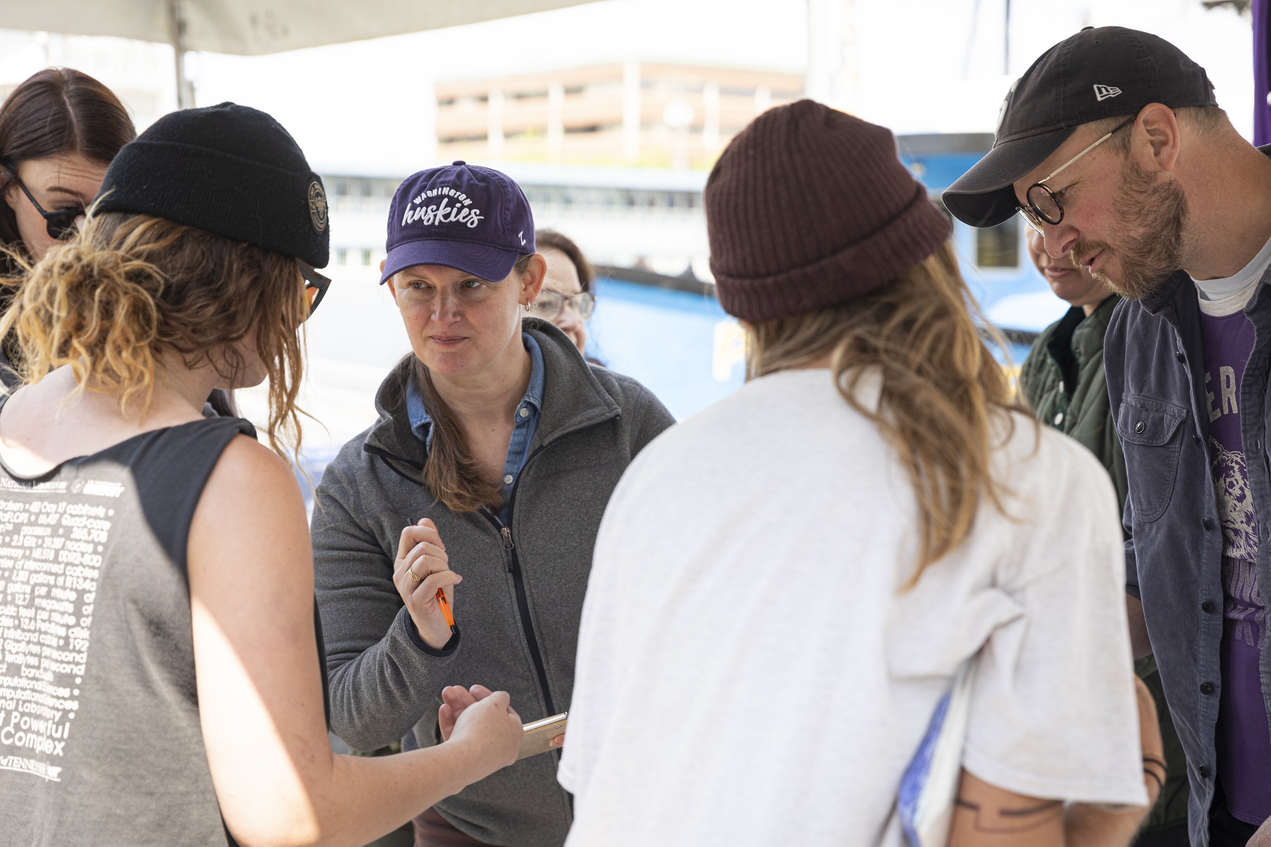 A group of people look at a central item and at each other under a tent at the Fisherman's Terminal.