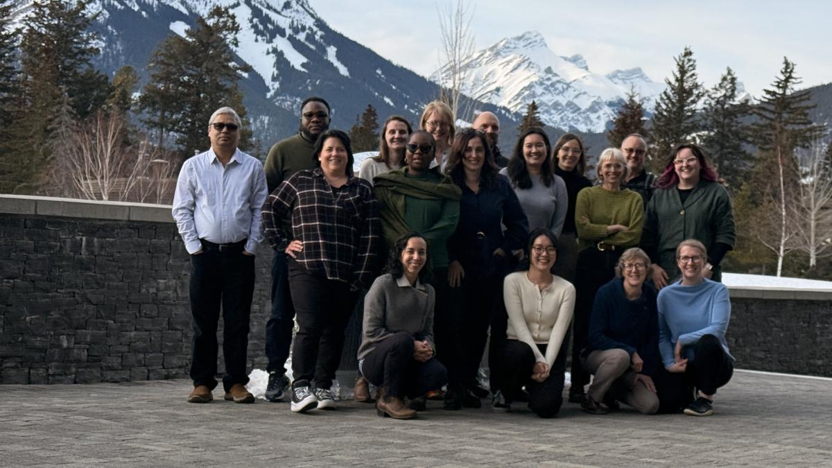 Seventeen people stand and pose in front of a scenic view of mountains and trees