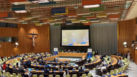 people gathered in a conference room with a large screen and panel of speakers