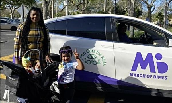 Mother and her two children stand in front of a parked car and smile