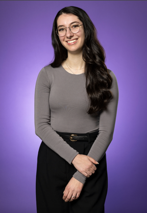 Young woman with long brown hair wearing glasses smiles poses and smiles for photo