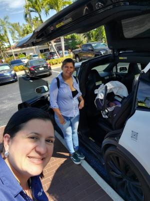 Two women smile next to a parked car with a baby in a carseat